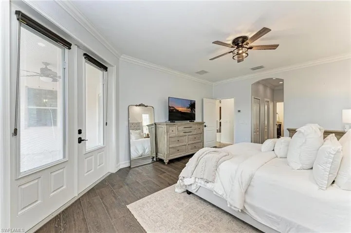Bedroom with crown molding, arched walkways, dark wood finished floors, ceiling fan, and a closet