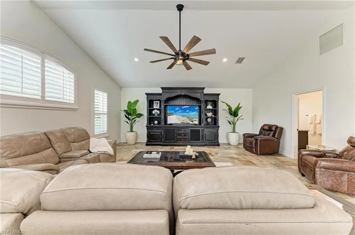 Living room featuring ceiling fan, lofted ceiling, stone finish flooring, and recessed lighting