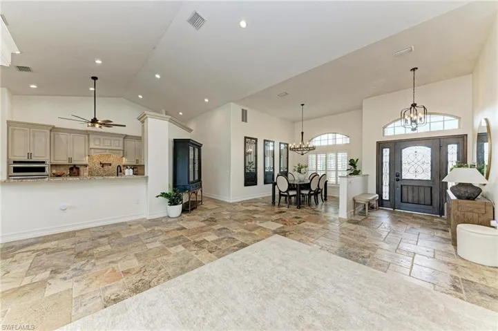 Foyer with stone tile flooring, vaulted ceiling, hanging lights, and a ceiling fan