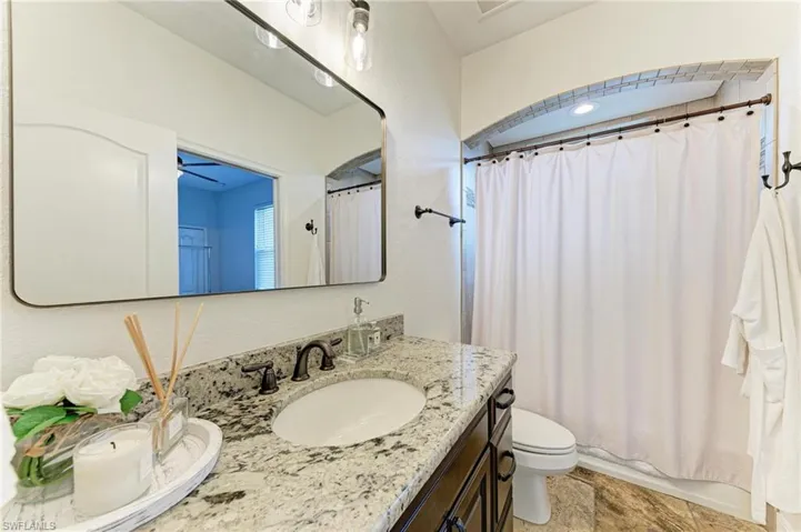 Full bathroom with vanity, a textured wall, shower / bathtub combination with curtain, and light stone finish floors