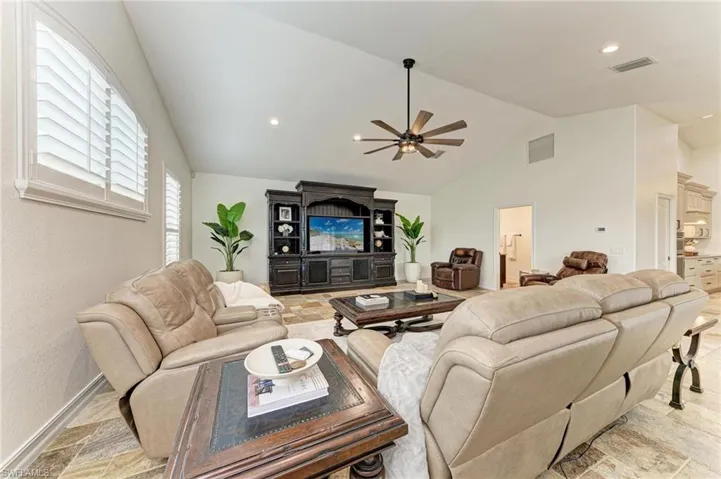 Living room with stone finish flooring, a ceiling fan, lofted ceiling, and recessed lighting
