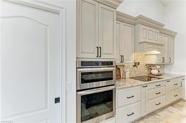 Kitchen with double oven, light stone counters, backsplash, cream cabinetry, and black electric stovetop
