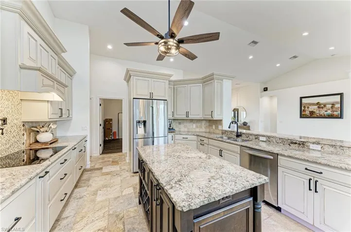 Kitchen featuring light stone countertops, a kitchen island, ceiling fan, stainless steel appliances, and two tone cabinets