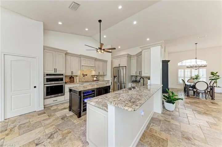 Kitchen with light stone counters, beverage cooler, a kitchen island, stainless steel appliances, and dual tone cabinetry