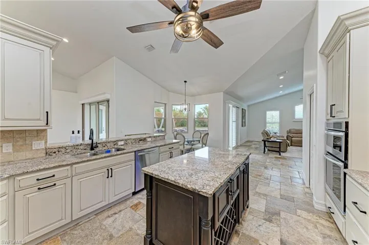 Kitchen with light stone counters, a ceiling fan, vaulted ceiling, open floor plan, and a kitchen island