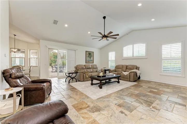 Living room featuring lofted ceiling, a ceiling fan, stone tile flooring, and suspended lighting
