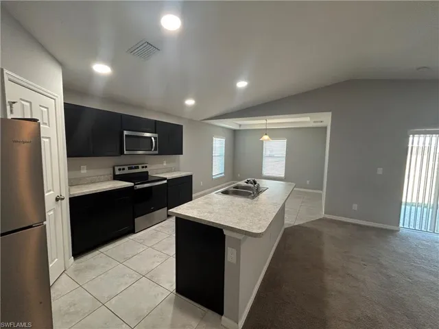 Kitchen with dark cabinetry, light countertops, stainless steel appliances, light tile patterned floors, and vaulted ceiling