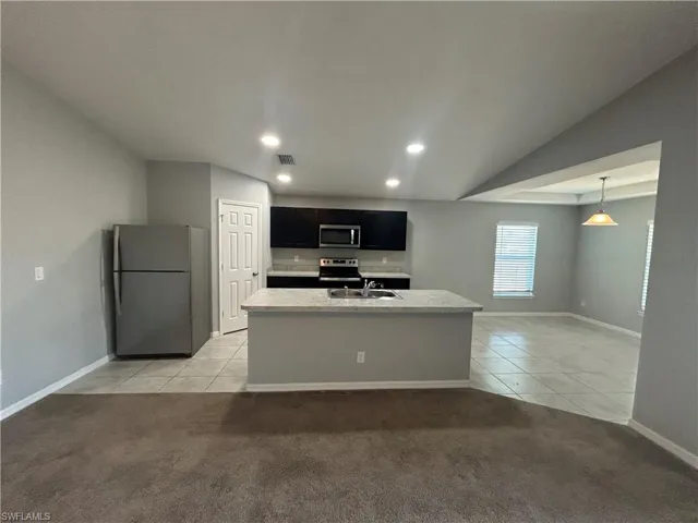 Kitchen with dark cabinets, stainless steel appliances, an island with sink, light colored carpet, and light tile patterned floors