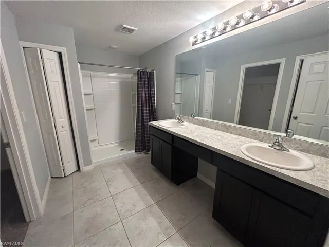 Bathroom with double vanity, a shower stall, a textured ceiling, a walk in closet, and light tile patterned floors
