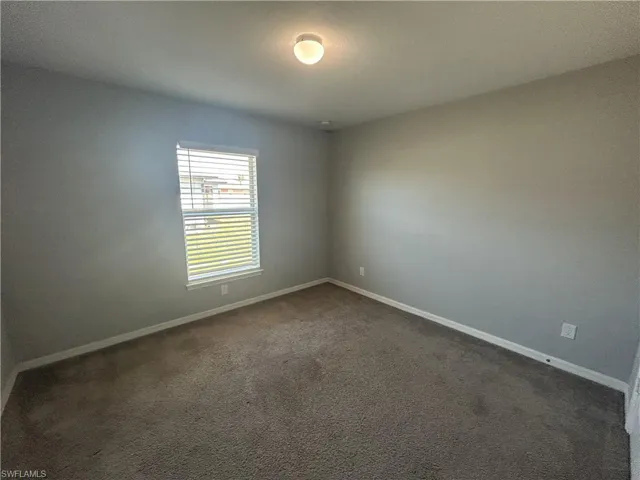 Spare room with dark carpet and baseboards