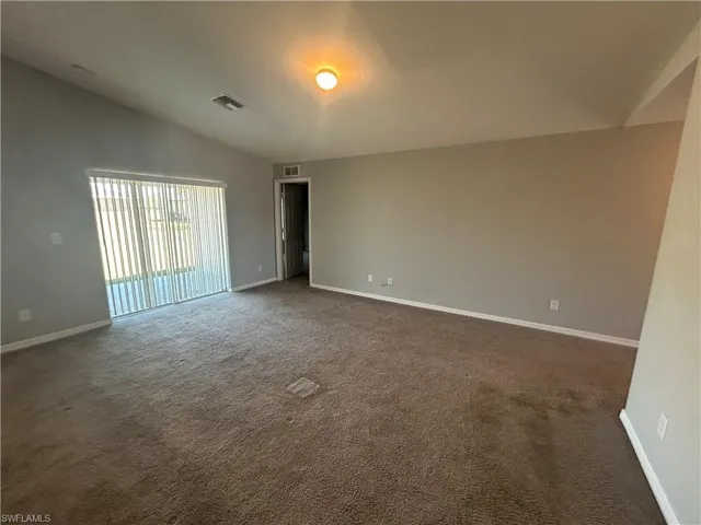Empty room with vaulted ceiling and dark carpet