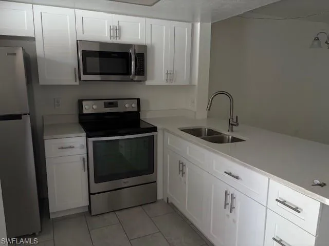 Kitchen with stove, refrigerator, light tile patterned floors, white cabinetry, and light countertops