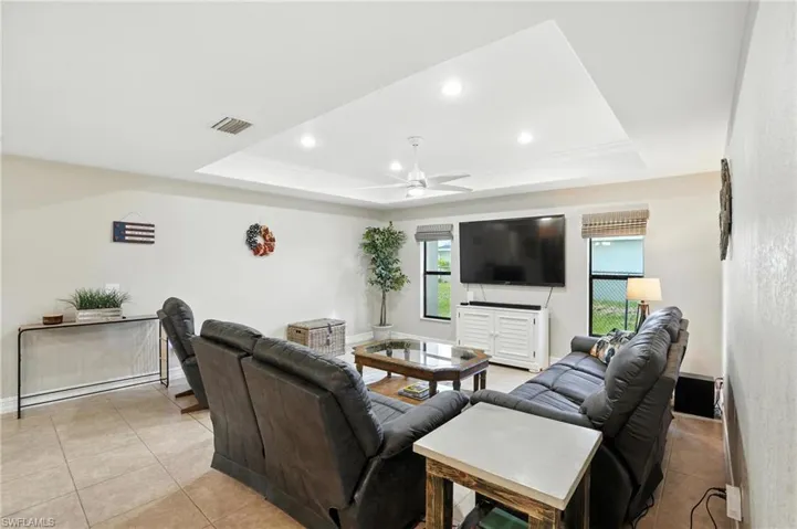 Living room with a raised ceiling, a ceiling fan, light tile patterned flooring, and recessed lighting