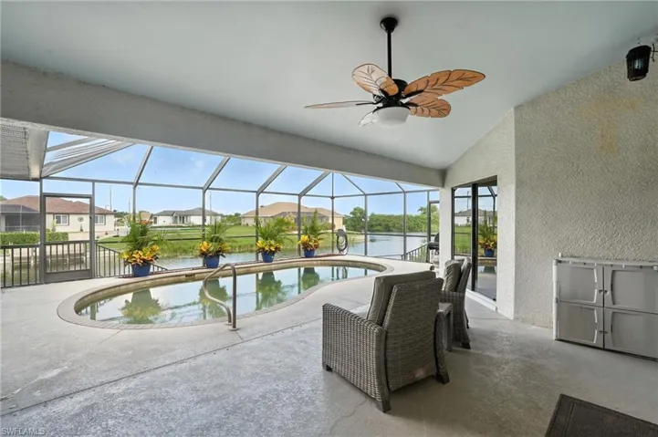 Swimming pool with a patio area, a water view, a residential view, ceiling fan, and glass enclosure