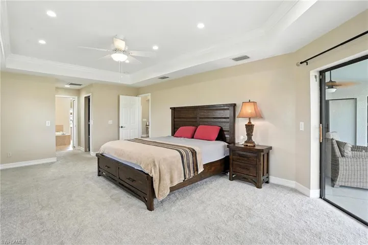 Bedroom featuring a raised ceiling, ornamental molding, light carpet, recessed lighting, and ceiling fan