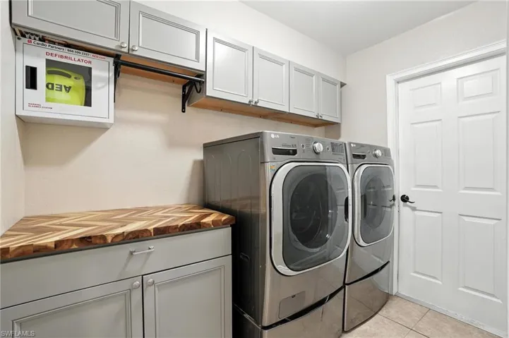 Washroom featuring washer and dryer, cabinet space, and light tile patterned floors