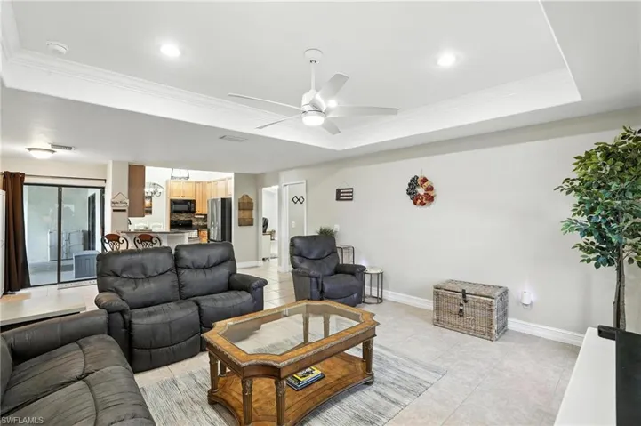 Living area with a raised ceiling, ornamental molding, ceiling fan, light tile patterned floors, and recessed lighting