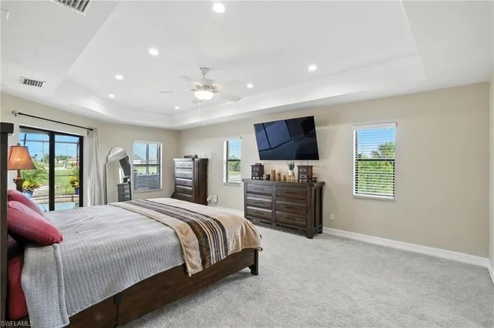 Bedroom with a raised ceiling, multiple windows, ornamental molding, recessed lighting, and light carpet
