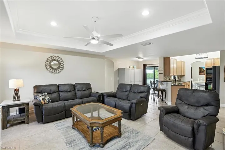 Living room with a tray ceiling, arched walkways, ceiling fan, light tile patterned floors, and ornamental molding