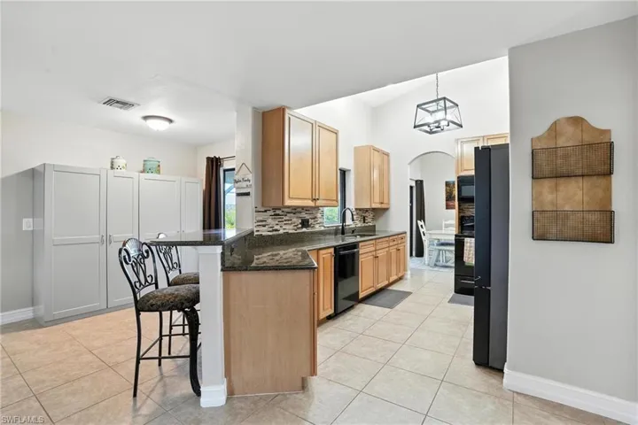 Kitchen featuring a kitchen breakfast bar, black appliances, arched walkways, light tile patterned floors, and a peninsula