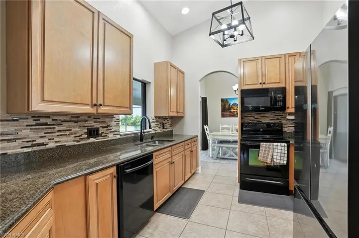 Kitchen featuring black appliances, arched walkways, tasteful backsplash, light tile patterned floors, and pendant lighting