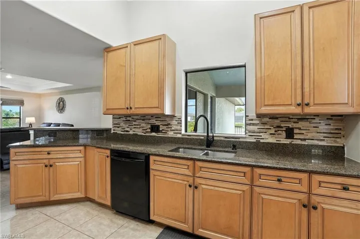 Kitchen with black dishwasher, backsplash, dark stone countertops, a peninsula, and crown molding