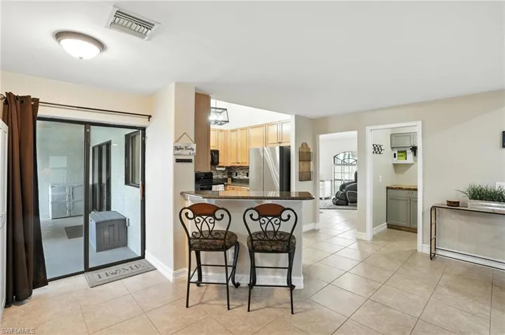 Kitchen featuring black appliances, a kitchen breakfast bar, dark countertops, light tile patterned floors, and decorative backsplash