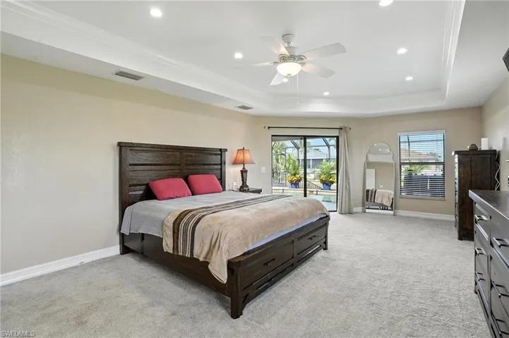 Bedroom featuring a tray ceiling, ornamental molding, recessed lighting, light carpet, and access to exterior