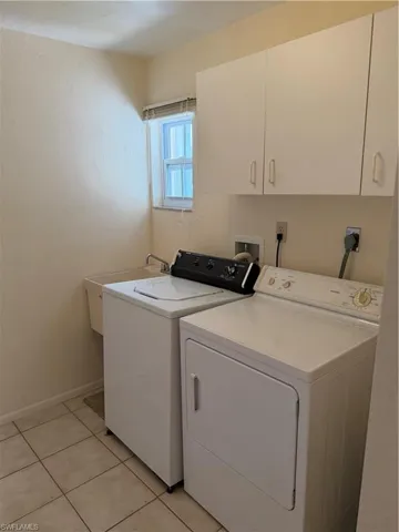 Laundry room featuring washing machine and dryer, light tile patterned floors, and cabinet space