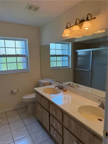 Full bathroom with a shower with door, double vanity, light tile patterned floors, and healthy amount of natural light