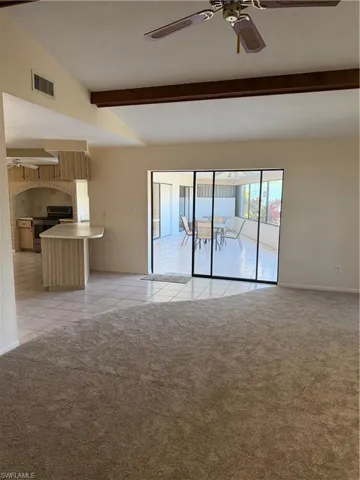 Unfurnished living room featuring ceiling fan, light colored carpet, light tile patterned floors, and lofted ceiling with beams