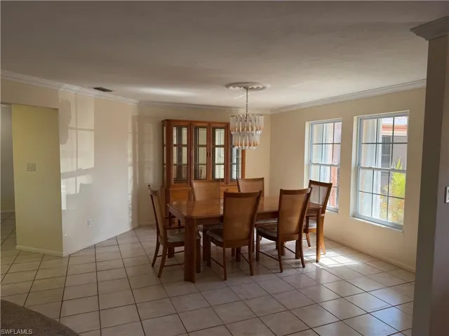 Dining room with light tile patterned floors, ornamental molding, and hanging lights