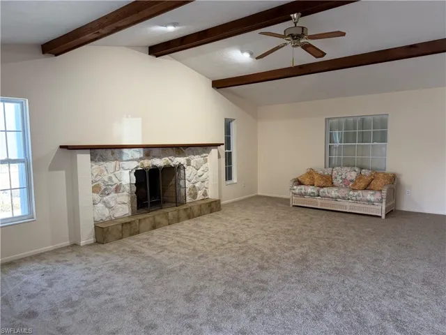 Unfurnished living room featuring a ceiling fan, carpet, and a stone fireplace