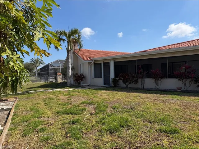 Back of house featuring a tiled roof, a lawn, a sunroom, and stucco siding