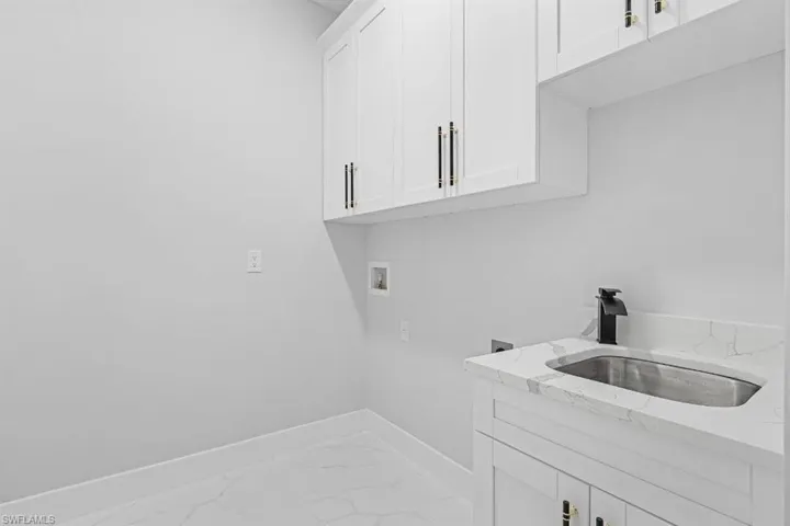Laundry area featuring marble look tiles, hookup for a washing machine, baseboards, and cabinet space