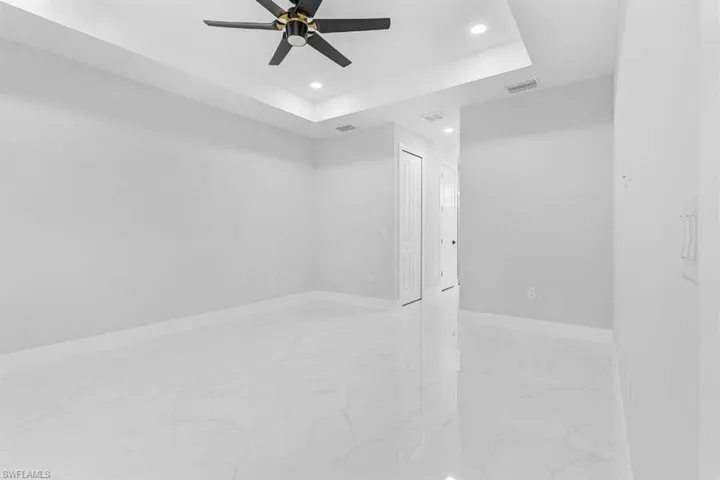 Unfurnished room featuring light marble finish flooring, recessed lighting, ceiling fan, baseboards, and a tray ceiling