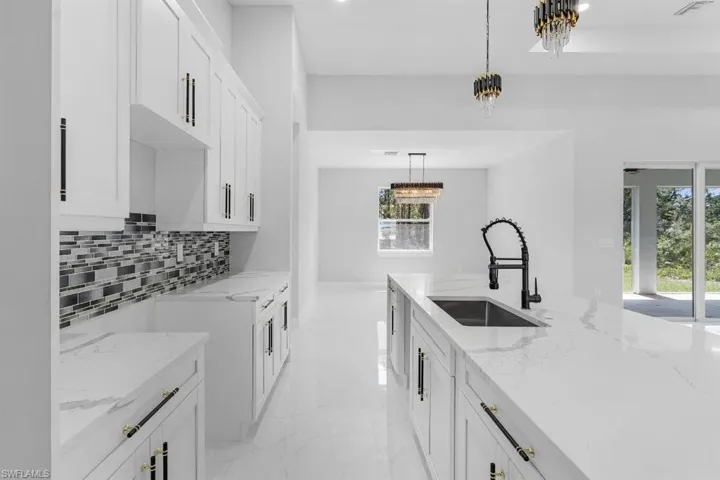 Kitchen with a sink, light marble finish flooring, tasteful backsplash, white cabinetry, and light stone countertops