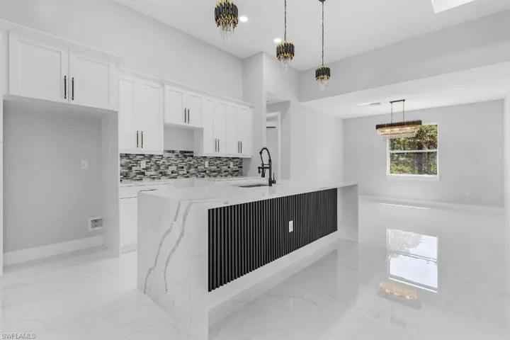 Kitchen with a sink, light marble finish flooring, white cabinets, light stone countertops, and an island with sink