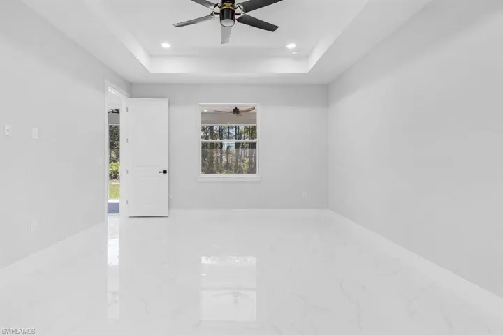 Unfurnished room with marble tiled floors, a ceiling fan, a tray ceiling, recessed lighting, and baseboards