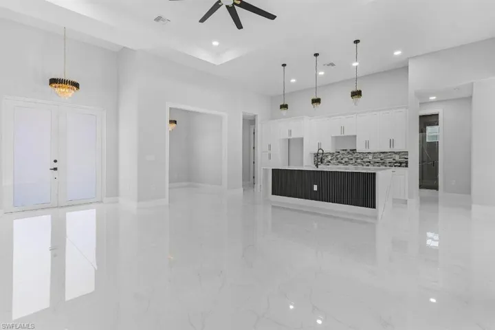 Unfurnished living room featuring a ceiling fan, recessed lighting, light marble finish flooring, baseboards, and a towering ceiling