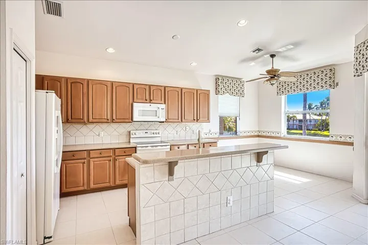 Kitchen with white appliances, tasteful backsplash, light tile patterned flooring, and visible vents