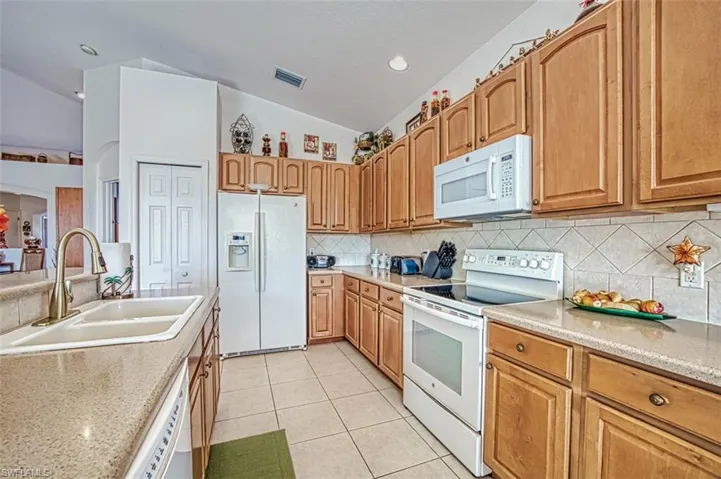 Kitchen with lofted ceiling, light stone counters, white appliances, and sink
