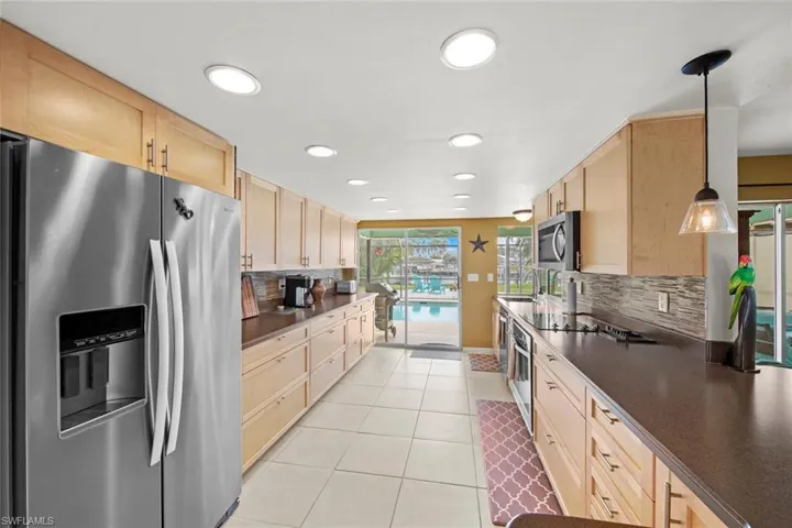 Kitchen featuring light brown cabinetry, backsplash, hanging light fixtures, and appliances with stainless steel finishes