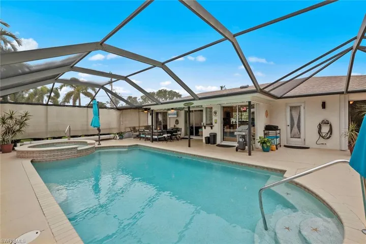 View of pool with a patio area, glass enclosure, and an in ground hot tub