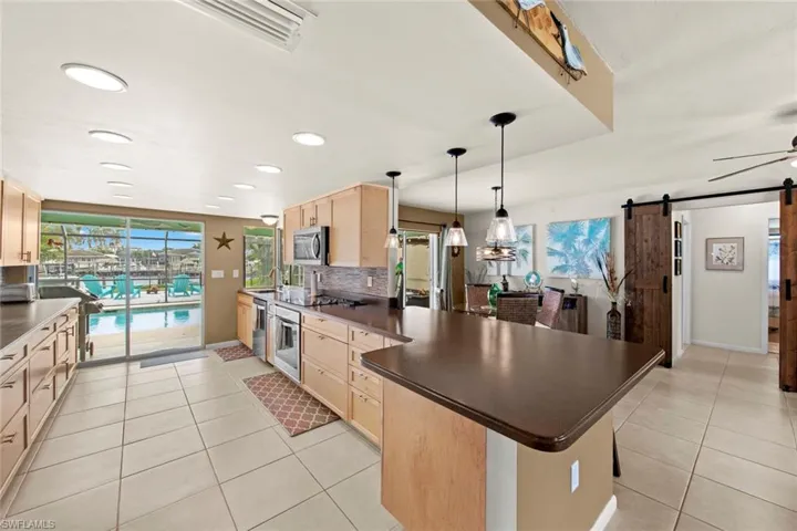 Kitchen with a barn door, decorative backsplash, stainless steel appliances, light tile patterned floors, and light brown cabinetry