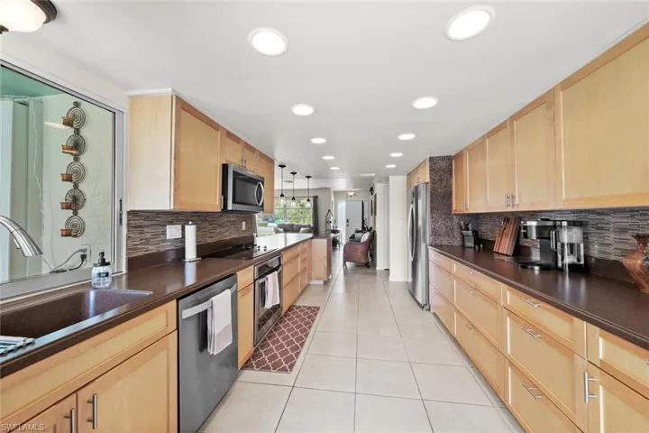 Kitchen with light brown cabinetry, light tile patterned floors, hanging light fixtures, and appliances with stainless steel finishes