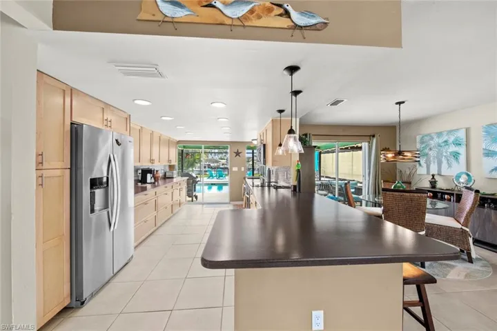 Kitchen featuring stainless steel refrigerator with ice dispenser, light brown cabinets, a kitchen breakfast bar, hanging light fixtures, and light tile patterned flooring