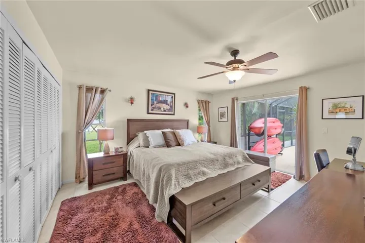 Bedroom featuring ceiling fan, multiple windows, light tile patterned floors, and access to outside