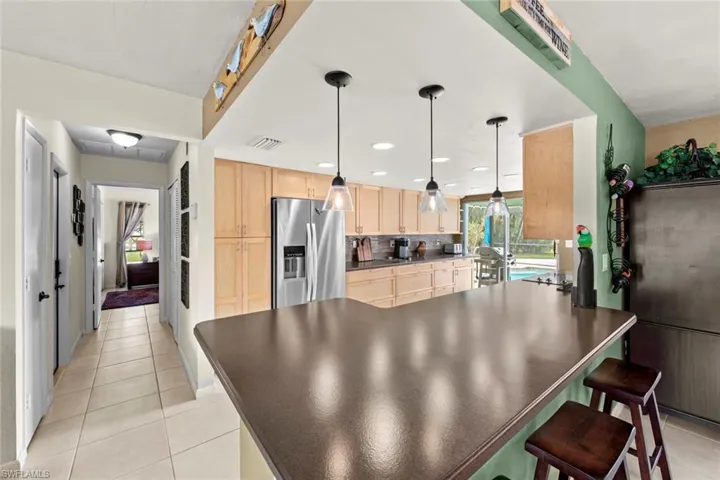Kitchen with decorative backsplash, hanging light fixtures, stainless steel fridge with ice dispenser, light tile patterned floors, and light brown cabinetry