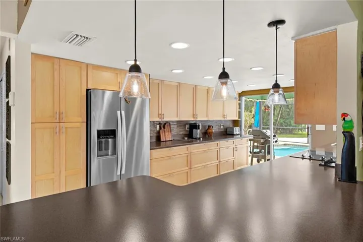 Kitchen featuring tasteful backsplash, light brown cabinetry, stainless steel fridge, and pendant lighting